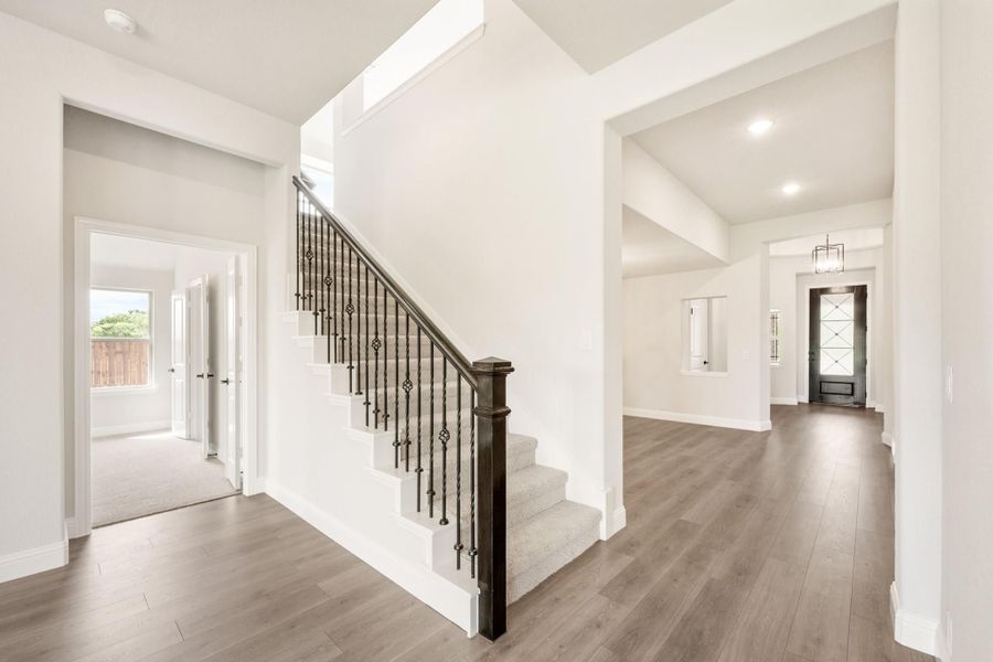 Bright home entryway with staircase featuring dark iron balusters and hardwood floors leading to front door