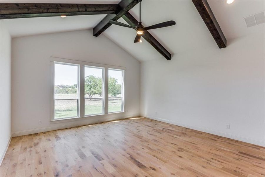 Primary bedroom featuring ceiling fan, light hardwood / wood-style flooring, beam ceiling, and a healthy amount of sunlight