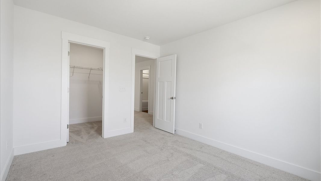 Notable secondary bedroom offering cozy carpeted flooring and a stylish walk-in closet at Iris Meadows