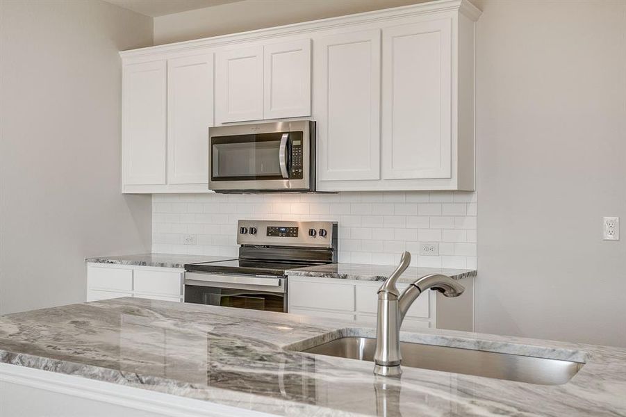 Kitchen with white cabinets, stainless steel appliances, and light stone countertops