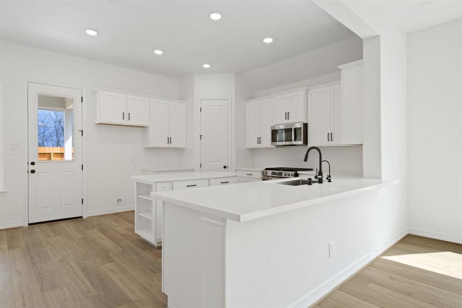 This light and bright kitchen features a large quartz island, white cabinets, a large sink overlooking your family room, recessed lighting, and beautiful backsplash.