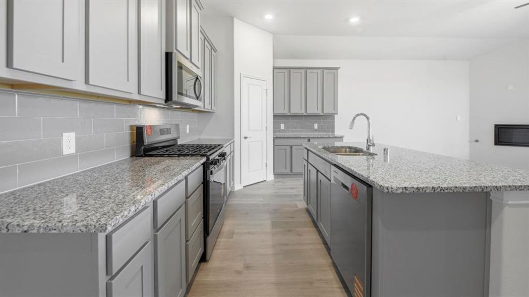 Kitchen featuring stainless steel appliances, gray cabinetry, light stone countertops, light wood-type flooring, and a kitchen island with sink Kitchen featuring stainless steel appliances, gray cabinetry, light stone countertops, light wood-type flooring, and a kitchen island with sink