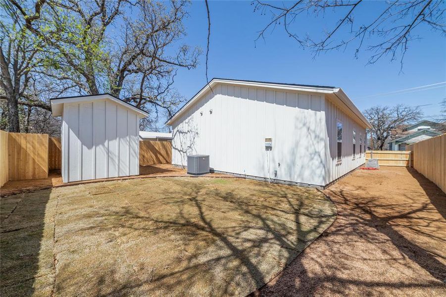 Back of property featuring an outdoor structure, a fenced backyard, board and batten siding, a storage unit, and central AC Back of property featuring an outdoor structure, a fenced backyard, board and batten siding, a storage unit, and central AC