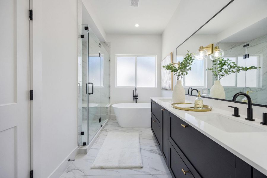 Luxurious primary bath featuring elegant marble finishes, a spacious glass-enclosed shower, a freestanding luxurious tub, and a double vanity with ample storage.