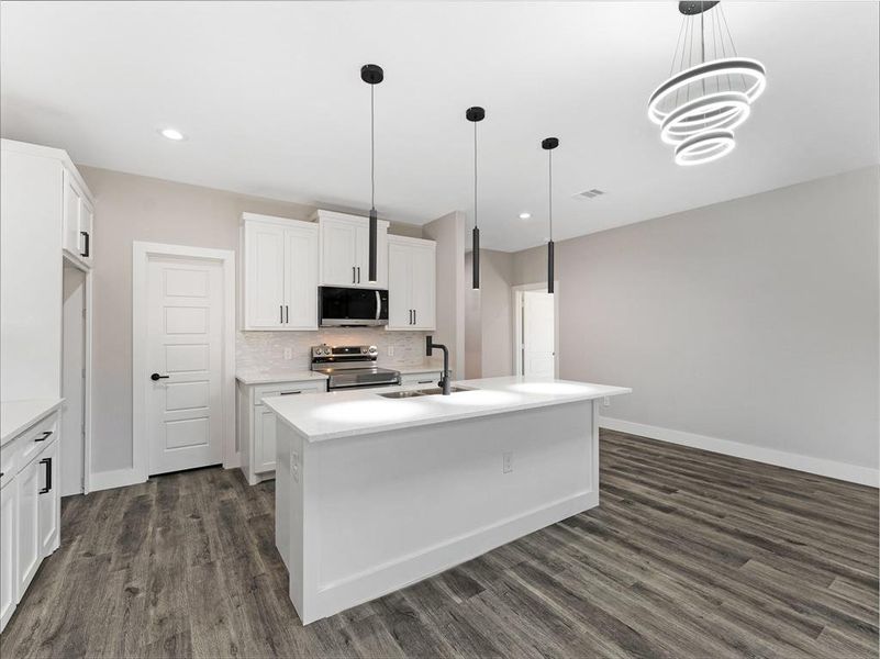 Kitchen with stainless steel appliances, sink, pendant lighting, white cabinetry, and an island with sink