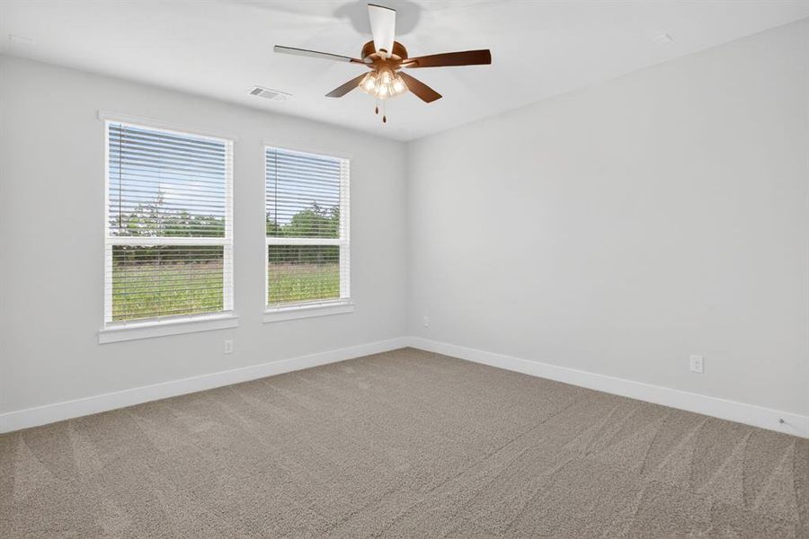 Carpeted room featuring two large windows with blinds, a ceiling fan with integrated lighting, and neutral wall tones Carpeted room featuring two large windows with blinds, a ceiling fan with integrated lighting, and neutral wall tones