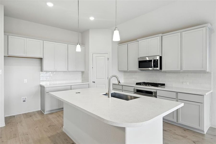 Kitchen featuring light countertops, light wood finished floors, tasteful backsplash, an island with sink, and recessed lighting Kitchen featuring light countertops, light wood finished floors, tasteful backsplash, an island with sink, and recessed lighting