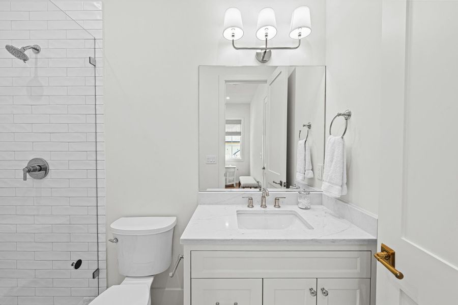 Serving secondary bedroom #1, this en suite bath features a clean, timeless design w/ a quartz countertop vanity, storage below & a Visual Comfort sconce. The shower includes a frameless glass enclosure, subway tile surround & herringbone-patterned tile flooring, paired w/ thoughtful details throughout. Serving secondary bedroom #1, this en suite bath features a clean, timeless design w/ a quartz countertop vanity, storage below & a Visual Comfort sconce. The shower includes a frameless glass enclosure, subway tile surround & herringbone-patterned tile flooring, paired w/ thoughtful details throughout.