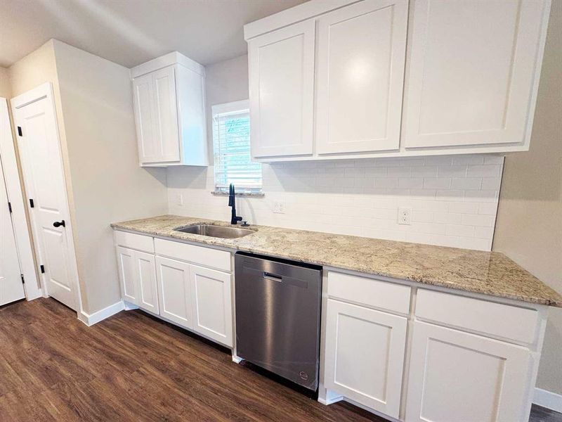 Kitchen featuring dark wood-type flooring, dishwasher, white cabinets, and a sink