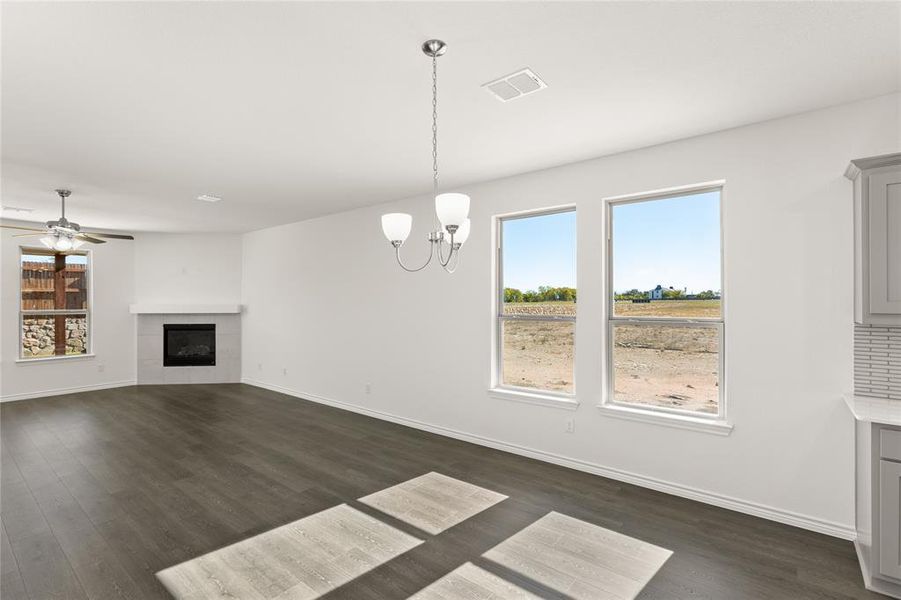 Unfurnished living room with a tiled fireplace, dark wood-type flooring, and ceiling fan with notable chandelier