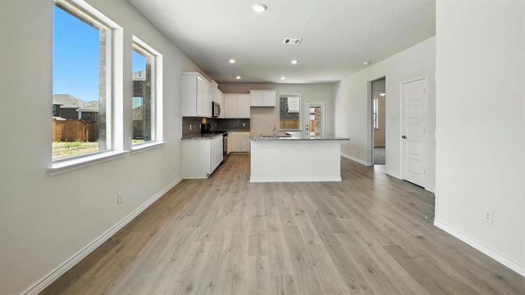 Kitchen featuring white cabinets, light wood finished floors, backsplash, an island with sink, and stainless steel appliances