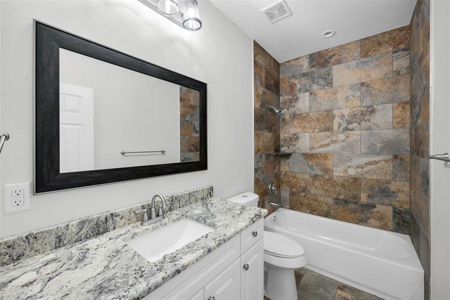 Full bathroom featuring vanity, toilet, visible vents, bathtub / shower combination, and stone finish flooring Full bathroom featuring vanity, toilet, visible vents, bathtub / shower combination, and stone finish flooring