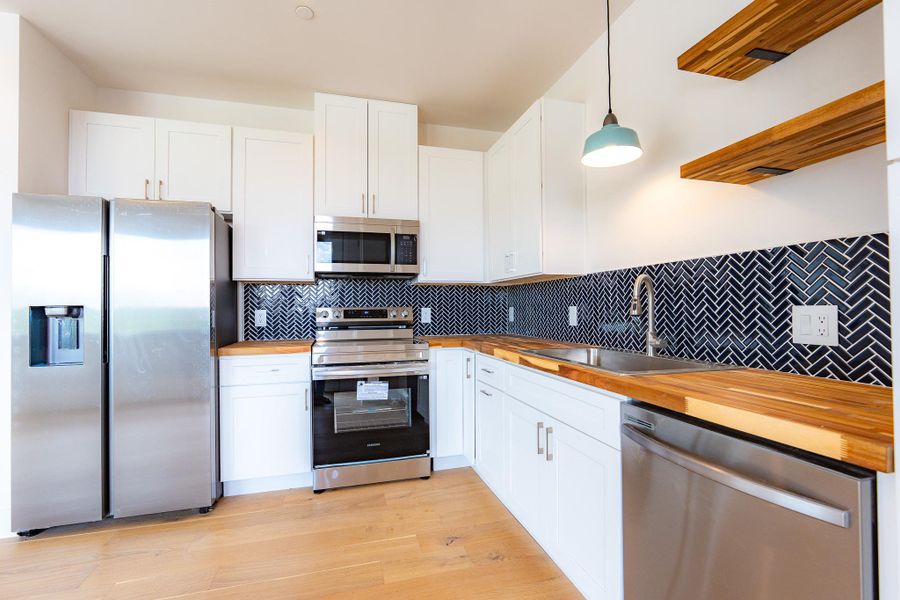 Culinary delights await in this bright and modern kitchen, showcasing butcher block countertops and a striking herringbone backsplash. Culinary delights await in this bright and modern kitchen, showcasing butcher block countertops and a striking herringbone backsplash.