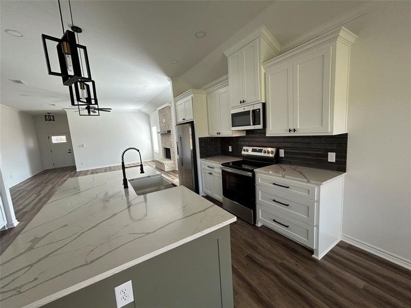 Kitchen featuring dark wood-style flooring, stainless steel appliances, hanging light fixtures, backsplash, and light stone countertops