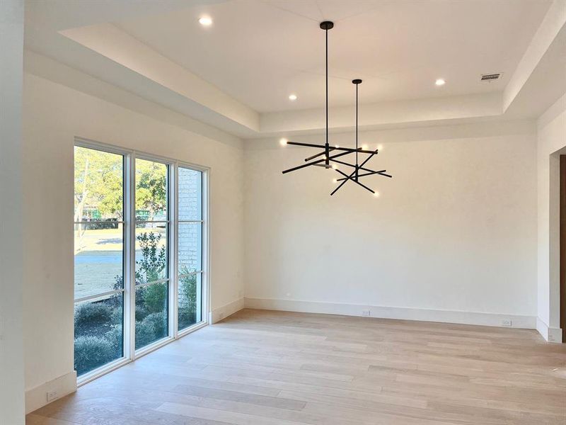 Unfurnished room with a raised ceiling, a notable chandelier, and light wood-type flooring