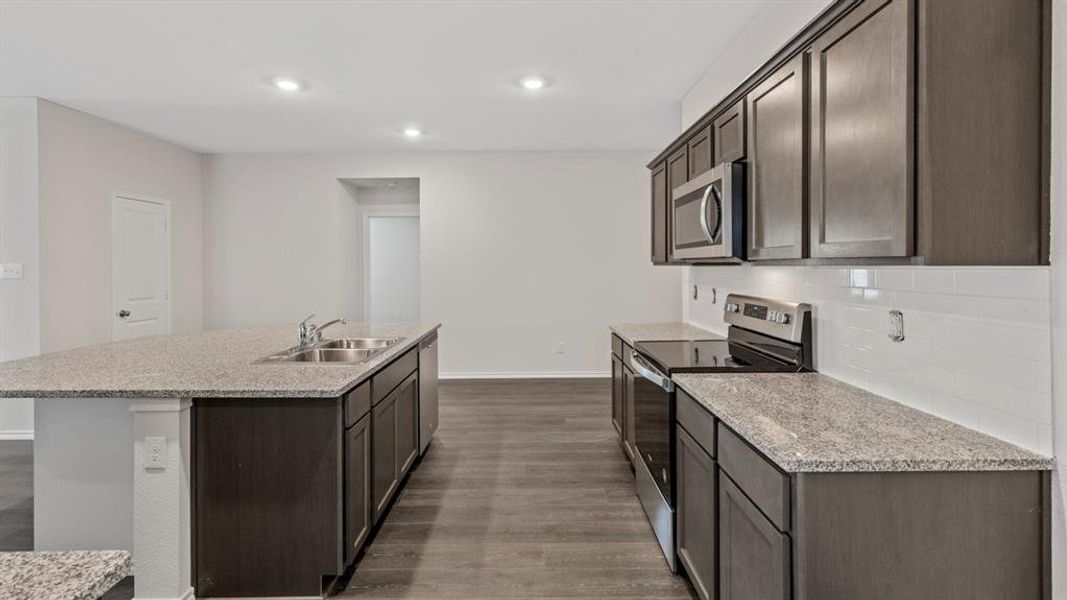 Kitchen featuring dark brown cabinetry, stainless steel appliances, light stone countertops, dark wood-type flooring, and recessed lighting