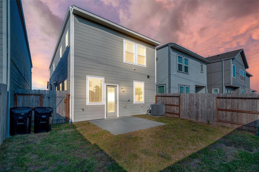 This photo showcases the backyard of a two-story home with a fenced yard, small patio, and grass area. The exterior is modern with neutral siding, and the space is perfect for outdoor activities.