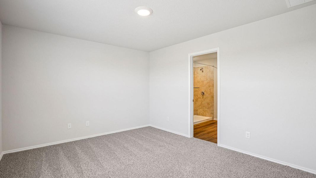 Carpeted room featuring a recessed ceiling light and an entryway to a full bathroom with a tiled shower and wood-finish flooring Carpeted room featuring a recessed ceiling light and an entryway to a full bathroom with a tiled shower and wood-finish flooring