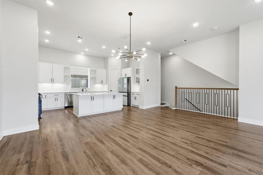 Expansive open-concept living area seamlessly connected to a modern kitchen with oversized island, sleek cabinetry, designer lighting, and stylish railing detail.