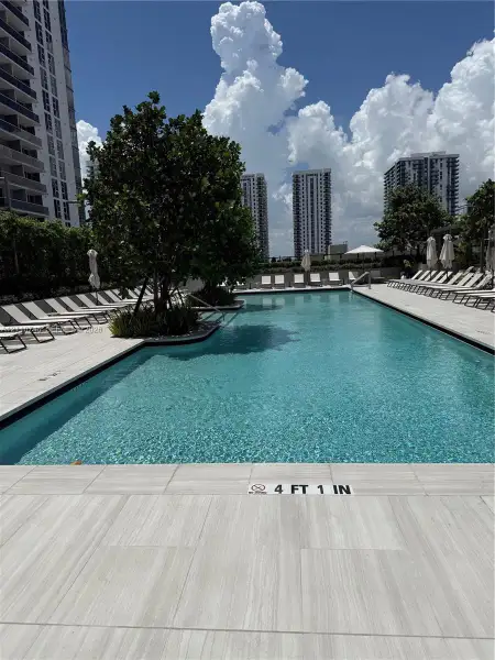 Swimming pool featuring light-toned tile decking, built-in planters with mature trees, and a rectangular perimeter