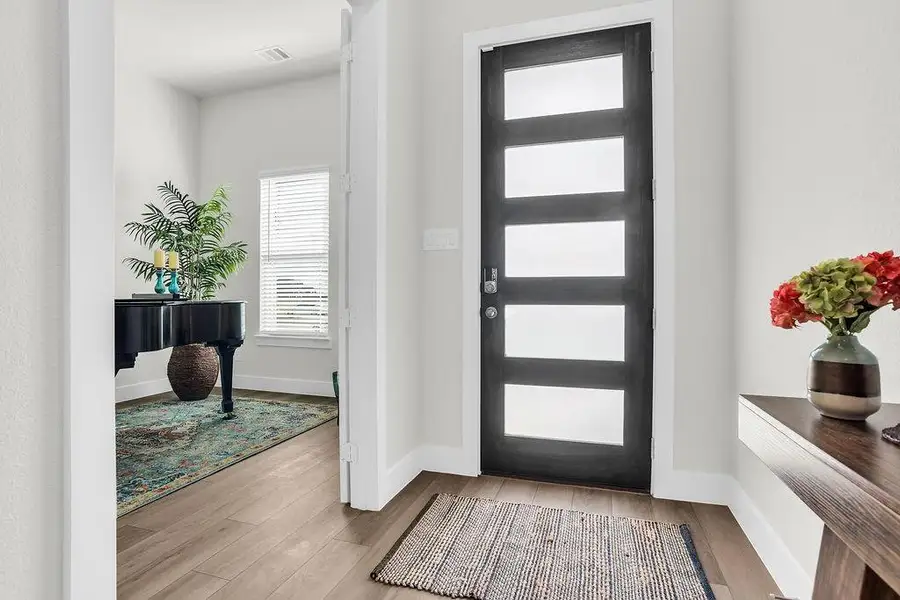 Modern entry door featuring frosted glass insets flooding the room with natural light, wood-finish flooring, and white trim throughout open to the study.
