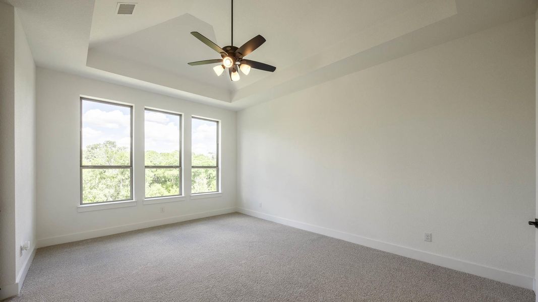 Empty room featuring a raised ceiling, light colored carpet, and a ceiling fan