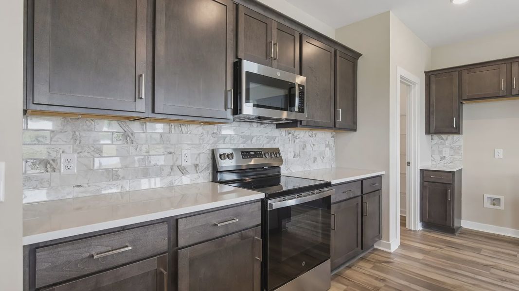 Kitchen with dark cabinetry, quartz countertops, stainless steel appliances, and tile backsplash Kitchen with dark cabinetry, quartz countertops, stainless steel appliances, and tile backsplash