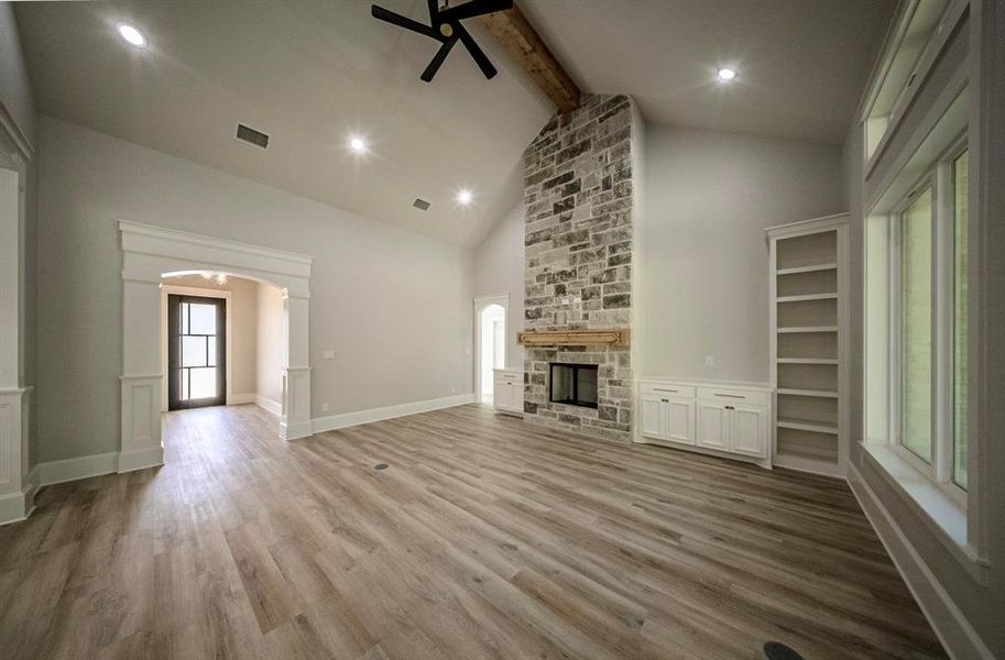 Unfurnished living room with a stone fireplace, beam ceiling, wood finished floors, a decorative wall, and recessed lighting Unfurnished living room with a stone fireplace, beam ceiling, wood finished floors, a decorative wall, and recessed lighting