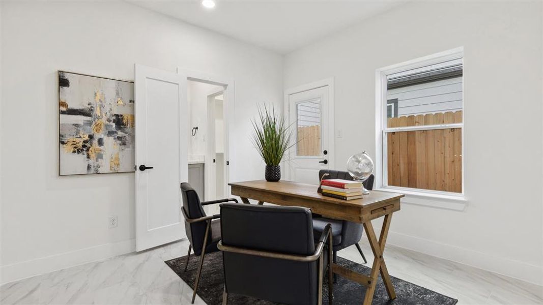 Modern, bright office space highlighted with clean lines, a large window for natural light, recessed lighting and sleek, marble-like tile flooring.