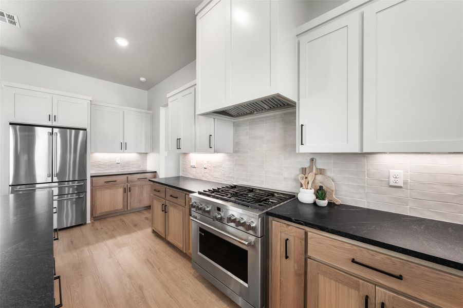 Kitchen featuring premium appliances, decorative backsplash, light wood-style floors, and white cabinets Kitchen featuring premium appliances, decorative backsplash, light wood-style floors, and white cabinets