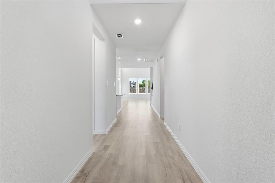 Hall featuring recessed lighting, light wood-style floors, and a textured wall Hall featuring recessed lighting, light wood-style floors, and a textured wall