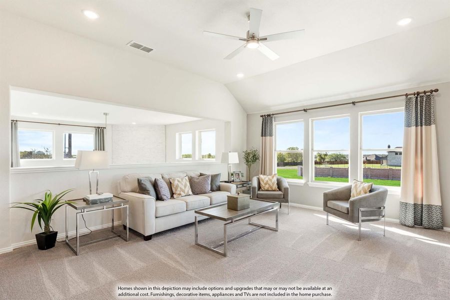 Bright living room with vaulted ceiling, ceiling fan, carpet flooring, and large windows overlooking a backyard