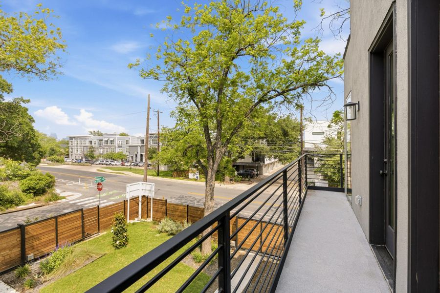 Balcony with black metal railings, a stucco exterior, and a black framed glass door, overlooking a fenced yard and streetscape