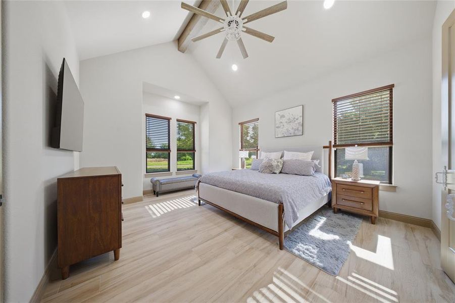 Spacious bedroom featuring light wood-finish flooring, a vaulted ceiling with a ceiling fan, recessed lighting, and multiple windows with wood blinds