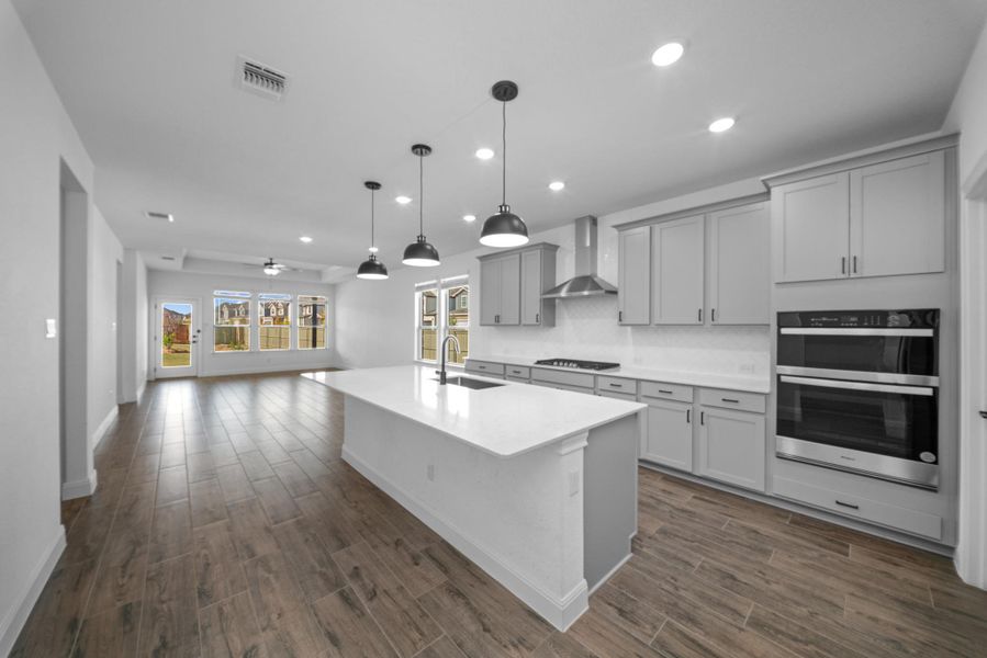 Kitchen featuring decorative backsplash, decorative light fixtures, stainless steel double oven, a ceiling fan, and dark wood-style flooring Kitchen featuring decorative backsplash, decorative light fixtures, stainless steel double oven, a ceiling fan, and dark wood-style flooring