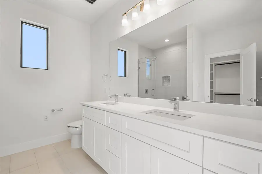 Bathroom featuring light tile patterned floors, healthy amount of natural light, double vanity, and a stall shower