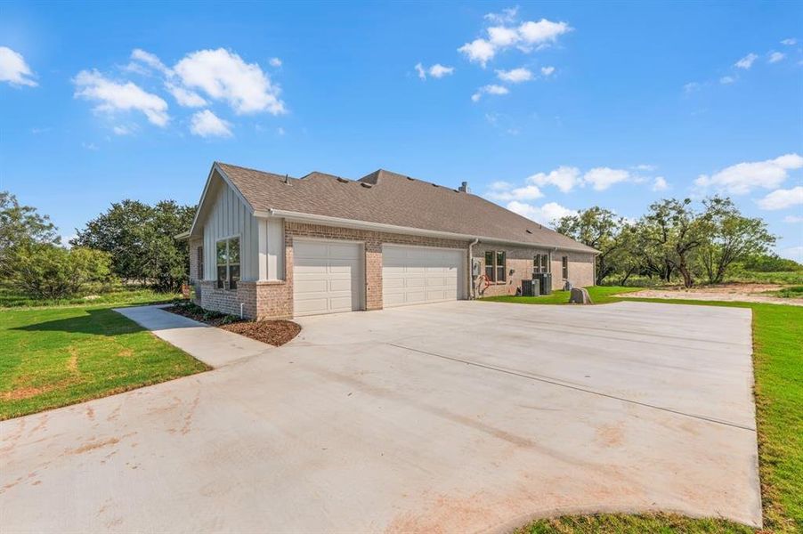 View of side of property with brick siding, a shingled roof, a yard, concrete driveway, and a garage