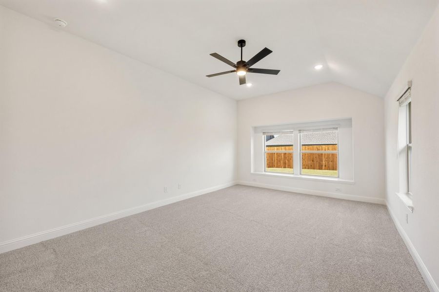 Empty bedroom with vaulted ceiling, ceiling fan, carpet flooring, and window overlooking backyard fence Empty bedroom with vaulted ceiling, ceiling fan, carpet flooring, and window overlooking backyard fence