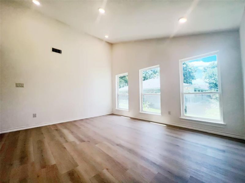 Spacious room featuring vaulted ceilings, recessed lighting, three large windows, wood-finish flooring, and white baseboards