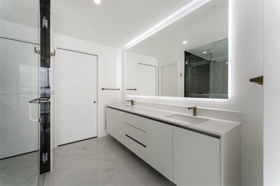 Spa-inspired primary bathroom featuring dual vanities, a deep soaking tub, a frameless glass rainfall shower, and designer porcelain tile throughout.