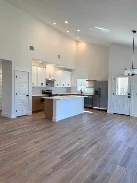 Kitchen featuring high vaulted ceiling, stainless steel appliances, white cabinetry, a kitchen island, and open floor plan