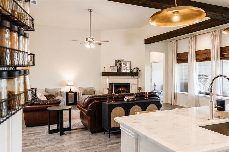 Open-concept living space featuring a stone-surround fireplace with a wood mantle, wood-finish flooring, and exposed wood beams