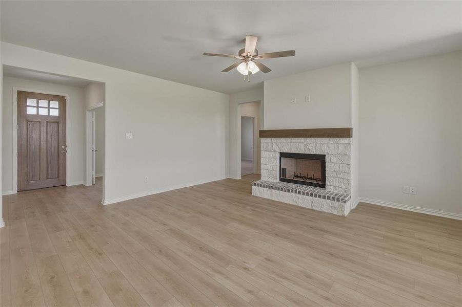 Spacious living area featuring wood-finish flooring, a stone fireplace with a wood mantel, and a ceiling fan with integrated lighting Spacious living area featuring wood-finish flooring, a stone fireplace with a wood mantel, and a ceiling fan with integrated lighting