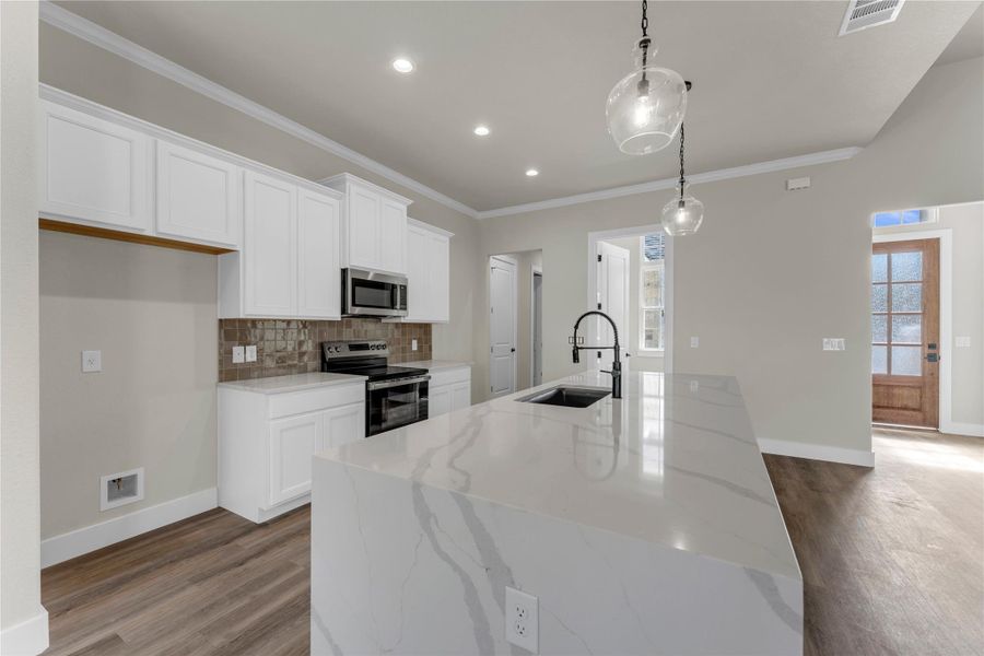 Kitchen featuring a center island with sink, white cabinetry, light stone counters, backsplash, and stainless steel appliances