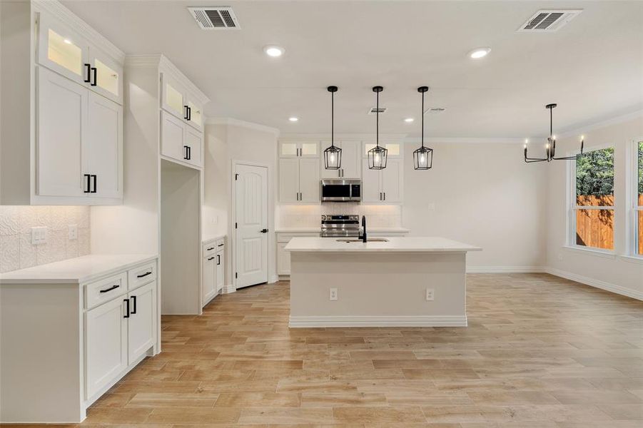 Kitchen with white cabinetry, decorative light fixtures, stainless steel appliances, and sink