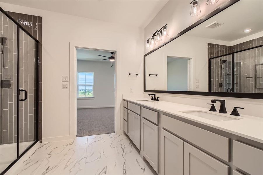 Full bath with marble look tiles, double vanity, a stall shower, a ceiling fan, and baseboards