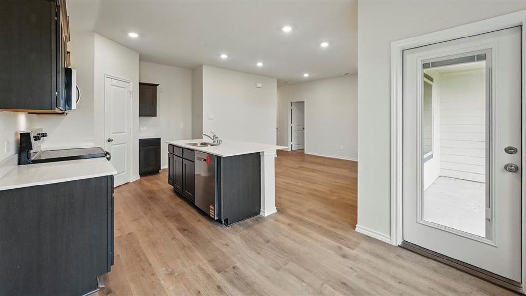 Kitchen with recessed lighting, a center island with sink, stainless steel appliances, light wood-style floors, and light stone countertops