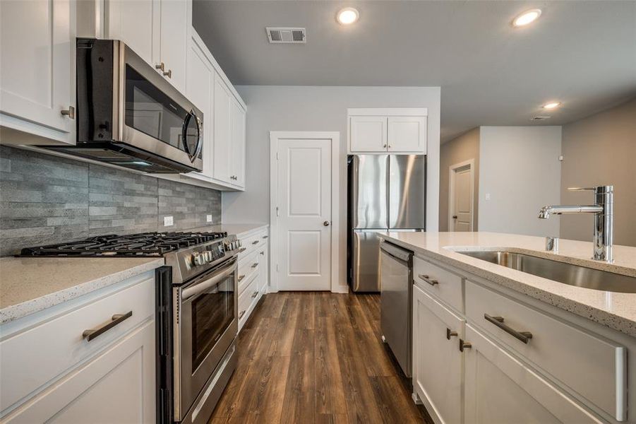 Kitchen with visible vents, a sink, dark wood finished floors, stainless steel appliances, and decorative backsplash