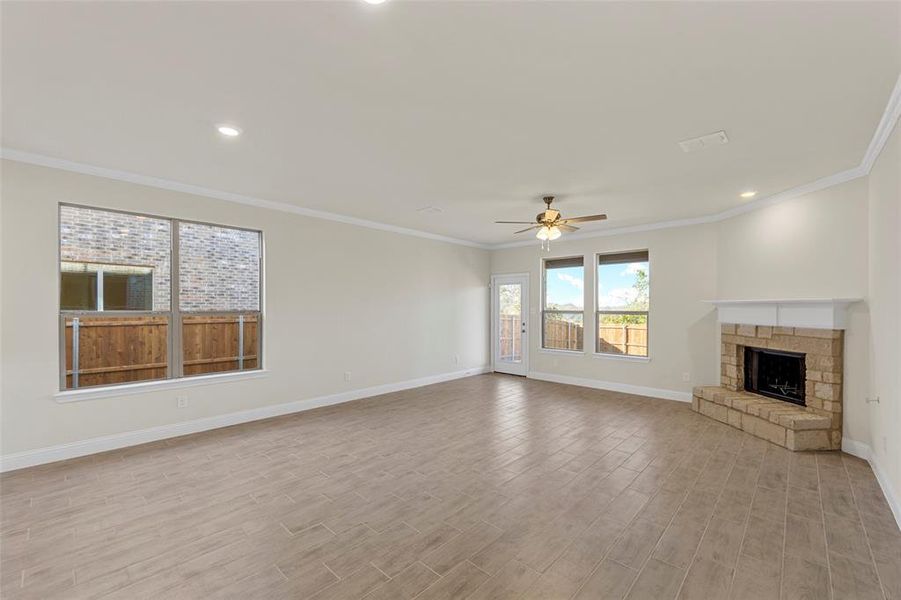 Unfurnished living room with a stone fireplace, crown molding, ceiling fan, and light hardwood / wood-style floors