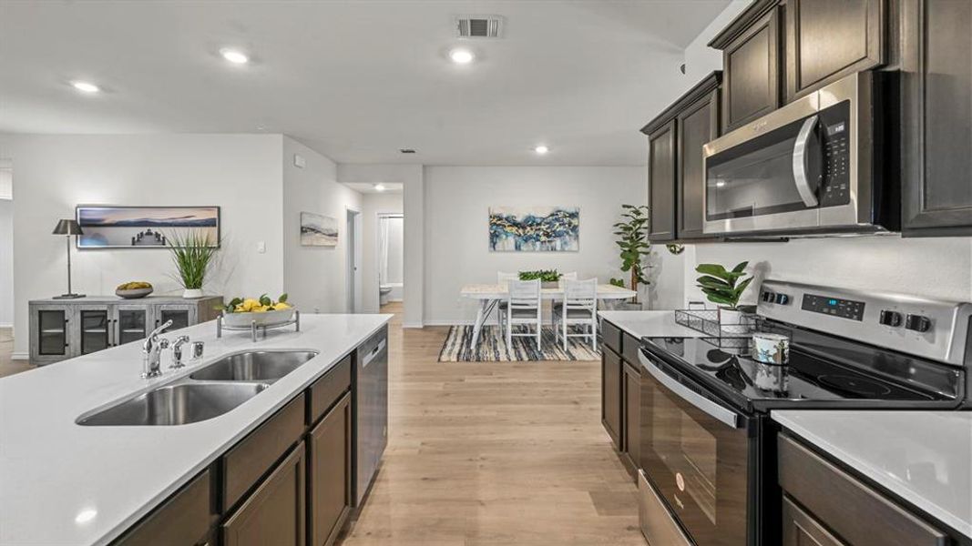 Kitchen featuring stainless steel appliances, light wood-style floors, dark wood finish cabinets, recessed lighting, and light stone countertops